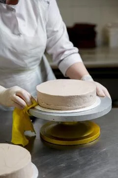 Baker prepares a cake on a turntable in a kitchen setup Stock Photos
