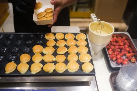 Baker preparing mini pancakes with strawberries in a busy kitchen during a Stock Photos