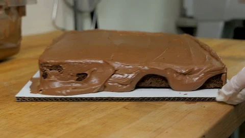 Baker pulls up frosting on the side of a chocolate cake Stock Footage 94242619