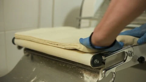 Baker puts the dough on the Dough sheeter Stock Footage 106473669