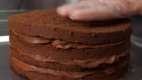 A baker puts the top onto a dark cake base with chocolate cream Vídeo Stock 103096508