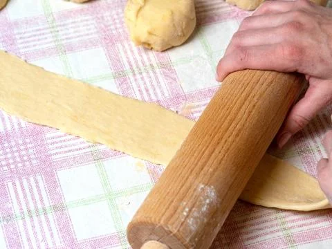 The Baker rolls the dough into strips on the kitchen table, sprinkled with fl Stock Photos