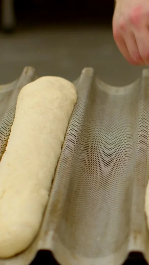 Baker scoring and pressing baguette dough in linen proofing mold under soft 動画素材 344575737