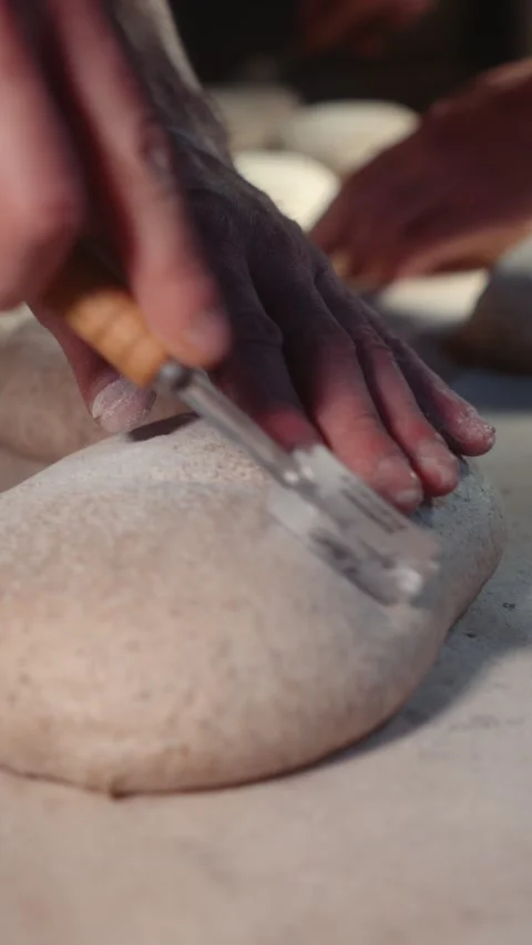 Baker scoring rye bread dough with a blade to create decorative patterns 스톡 동영상 344312925