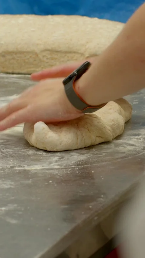 Baker shaping dough on floured stainless steel counter in commercial kitchen Video stock 345601492