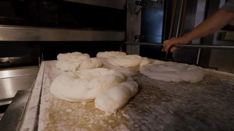 Baker shaping dough into rolls on a floured surface, with a commercial oven in Stock Footage 340172363
