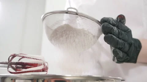 Baker sieves flour with strainer over bowl in kitchen close Stock Footage 137932064