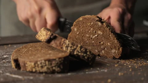 Baker slicing fresh whole grain rye bread with seeds on wooden cutting board Stock Footage 329966658
