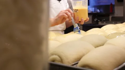 Baker spreading egg wash on bread loafs prior to cooking 库存影片 203896918
