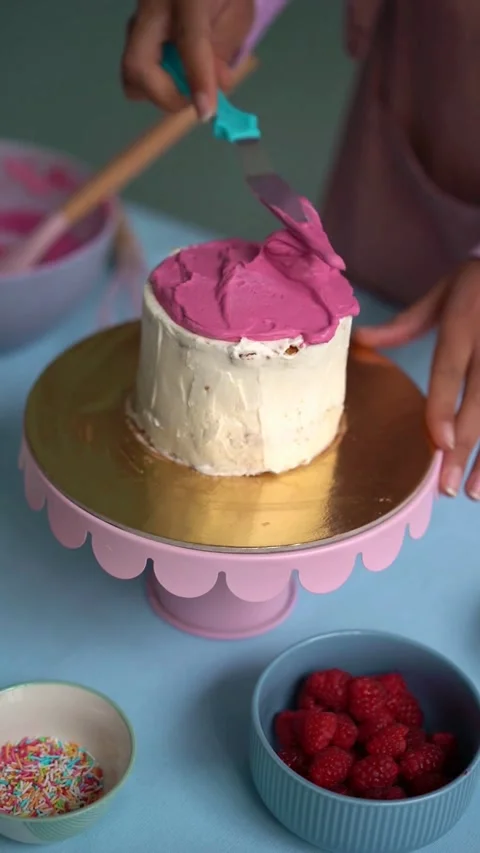 Baker spreading pink frosting on mini cake with spatula Stock Footage 331772465