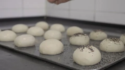 Baker sprinkling raw burger buns with sesame, poppy and chia seeds Stock Footage 251364047