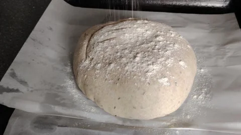 Baker sprinkling white flour over raw sourdough bread dough on parchment paper b Stock Footage 334592428
