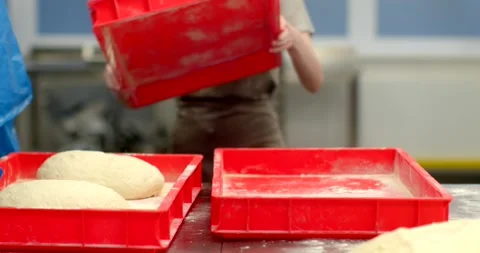 Baker stacking red proofing trays beside flour-dusted dough on stainless counter Stock-Footage 344582833