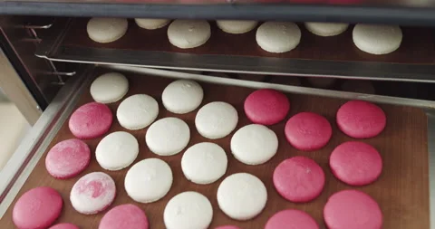 The baker takes out cooked macarons. Young cheerful girl confectioner in the Stock Footage 150264954
