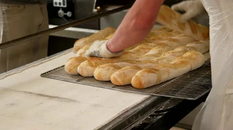 Baker taking out hot fresh baguettes to the tray Stock Footage 64471113