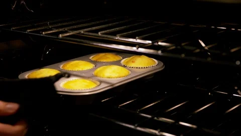Baker taking out metal cupcake tray from oven baking rack B Stock Footage 111677102