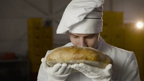 Baker in uniform sniffs a freshly baked loaf of bread, has a pleasure and looks Video stock 147258562