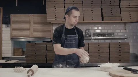 Baker unrolls dough with hands with rolling pin, young chef cook pizza for Stock Footage 72396019