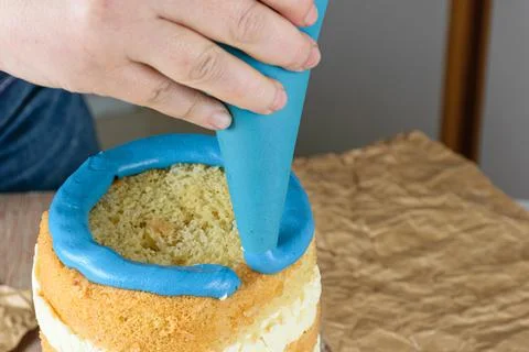 Baker using a icing nozzle to put blue frosting on top of cake. Stock Photos