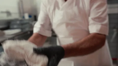 Baker in white shirt uses gloved hands to shape dough pieces in a commercial Stock Footage 331755332