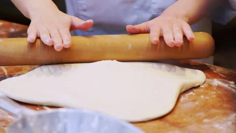 Baker in white uniform rolls raw dough piece on wooden table Video stock 133243412
