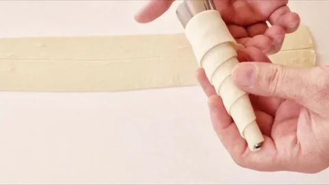 Baker wrapping puff pastry strips around a metal cone mold to make cream horns Stock Footage 327259611