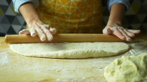 The baker in yellow apron rolls out the dough with a rolling pin Stock Footage 220227604