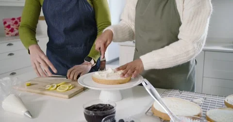 Bakers at counter placing cake layer slicing lemons spooning jam and smoothing Stock Footage 344681465