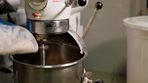 The Baker's hand opens and pours flour into the bowl of a large industrial mixer Stock-Footage 106458426