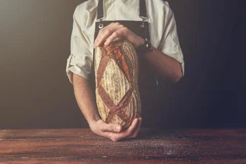 Baker's hands hold an oval bread. Stock-Fotos