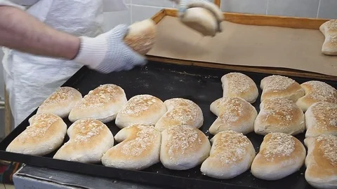Baker's hands over a cluster of baked bread buns on a wooden countertop Stock Footage 83793214