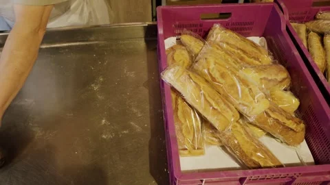 Baker's hands placing packaged bread loaves into pink crates on a stainless Stock Footage 340172420