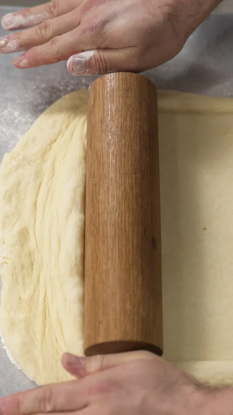 Bakers hands rolling out dough with a wooden rolling pin on a floured work Stockbeeldmateriaal 319040258