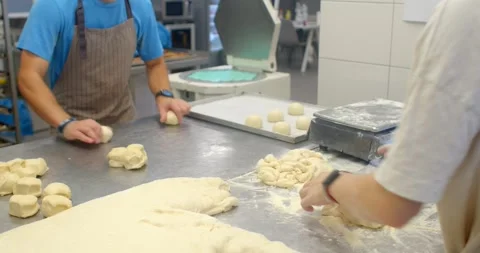 Bakers shaping dough and arranging buns on stainless steel prep table in, with Stock Footage 344595968