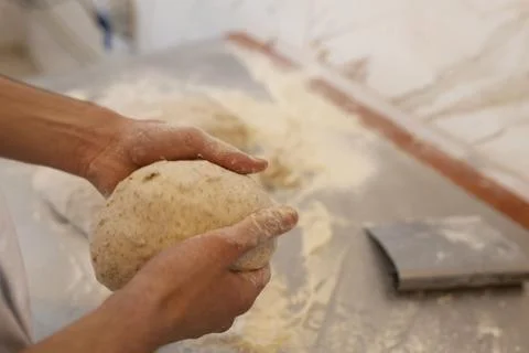 Bakers shaping raw bread dough by hand on floured table in bakery kitchen Fotos Stock