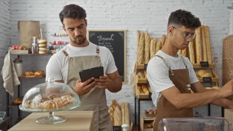 Bakers work in a bakery, one using a tablet while the other arranges pastri.. Stockbeeldmateriaal 289691052