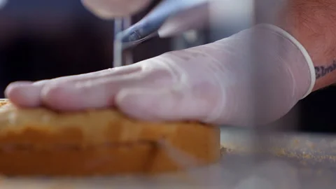 A bakery chef with gloved hand guides a cake leveler, slicing through a sin.. Vídeo Stock 296124595