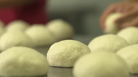 Bakery dough balls on table. Baker rolls more in the BG in slow motion Stock Footage 128461450