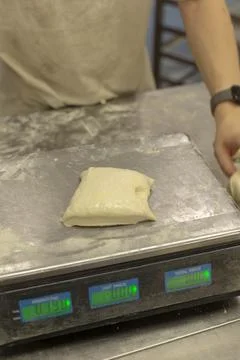 Bakery dough portion on stainless scale with baker blurred in background scene Stock Photos