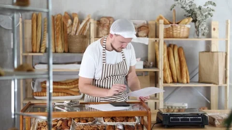 Bakery employee in apron examines documents, ponders debt restructuring Stock Footage 308420711