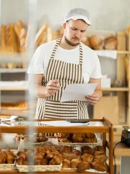 Bakery employee in apron examines documents, ponders debt restructuring Stockfoto's