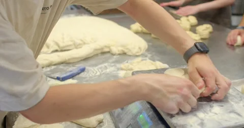 Bakery hands shaping and portioning dough on floured stainless table in, with Stock Footage 344597084