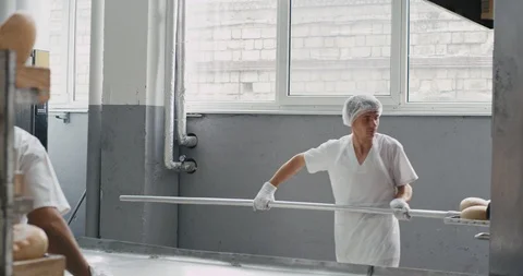Bakery worker equipped in a white uniform take the bread from industrial oven Stock Footage 112142396