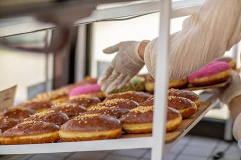 Bakery worker in gloves arranging assorted donuts on a tray. Stock Photos