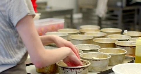 Bakery worker hands filling multiple round metal tins with egg in commercial Stock Footage 344583351