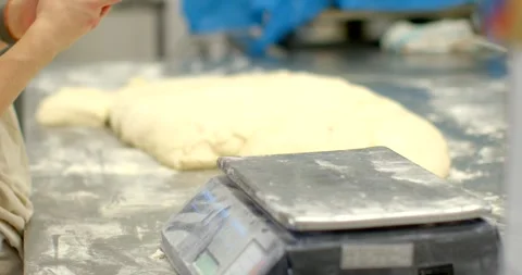 Bakery worker referencing smartphone over dough beside flour-dusted weighing Stock Footage 344595847