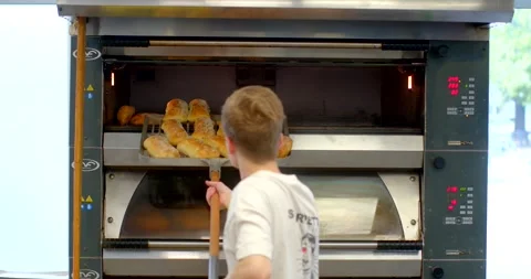 Bakery worker removing tray of golden rolls from industrial oven at eye level Stock Footage 344595923