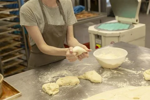 Bakery worker shaping dough by hand on floured stainless table in kitchen prep Stock Photos