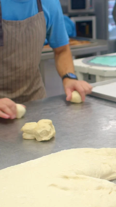 Bakery worker shaping dough on stainless steel prep counter in vertical view Stock Footage 344574380