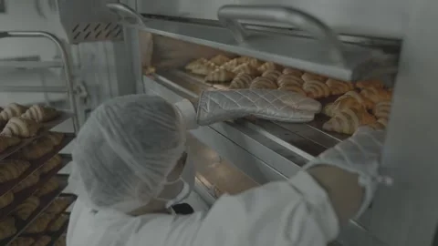 Bakery worker unloading hot trays of croissants from a deck oven. 스톡 동영상 327355312